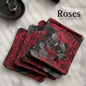 May include: Four red and black fabric coasters with a rose and spiderweb design. The coasters are stacked on top of each other. The text "Roses" is written in white letters on a white background.