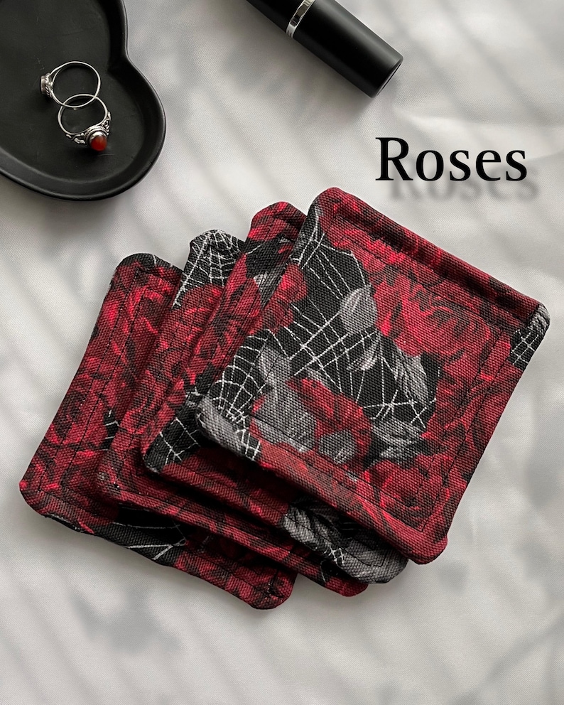 May include: Four red and black fabric coasters with a rose and spiderweb design. The coasters are stacked on top of each other. The text "Roses" is written in white letters on a white background.