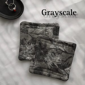 May include: Two grey and white fabric coasters with a floral pattern. The coasters are made of a soft, textured fabric and have a subtle sheen.