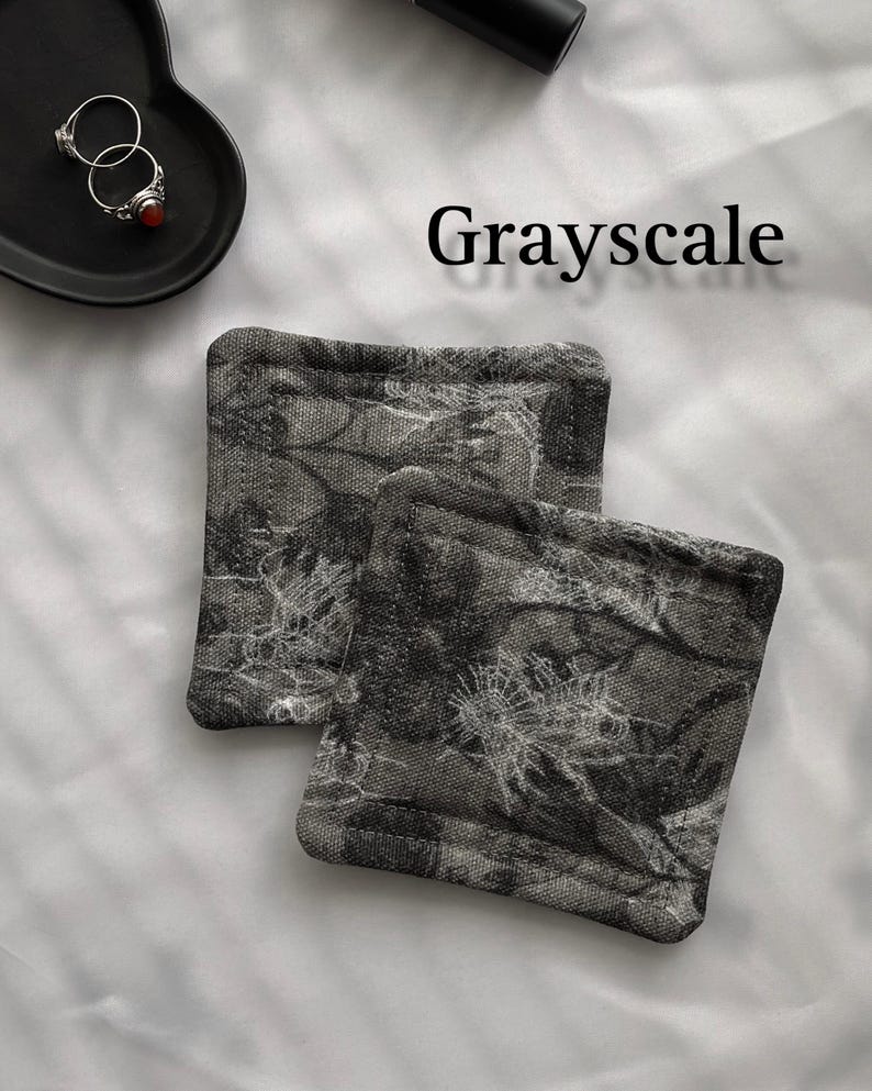 May include: Two grey and white fabric coasters with a floral pattern. The coasters are made of a soft, textured fabric and have a subtle sheen.