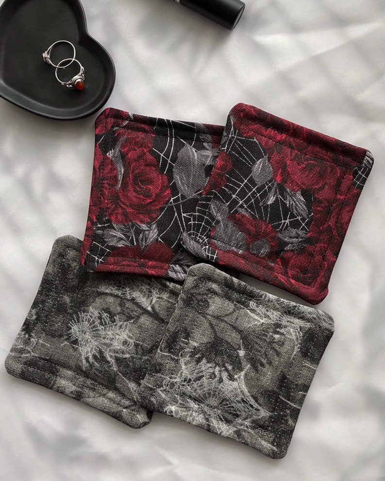 May include: Four square fabric coasters with a black background and a white spiderweb design. Two coasters feature red roses with a black background and a white spiderweb design.