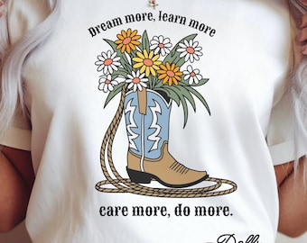May include: White t-shirt with a graphic of a cowboy boot filled with flowers. The boot is light brown and blue, with a rope and the text "Dream more, learn more, care more, do more." The shirt also has the name "-Dolly."