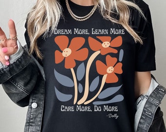 May include: Black t-shirt with a floral design and the text "Dream More, Learn More, Care More, Do More - Dolly".