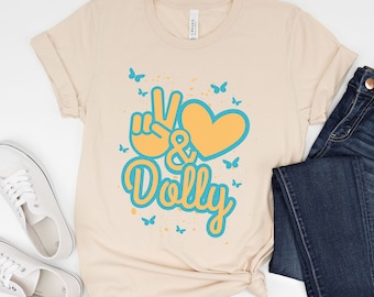 May include: A beige t-shirt with a peace sign, heart, and the text "& Dolly" in blue and yellow. The design is surrounded by blue butterflies.