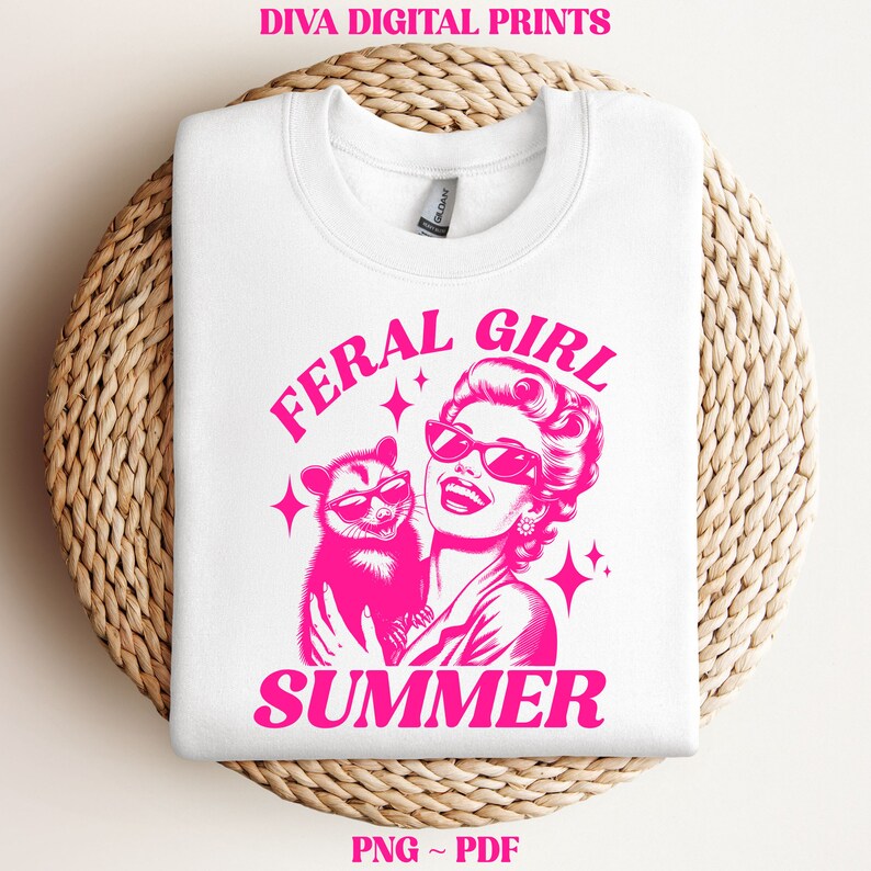 May include: A white t-shirt with a pink graphic design featuring a woman with sunglasses holding a possum. The text "Feral Girl Summer" is written in pink letters.