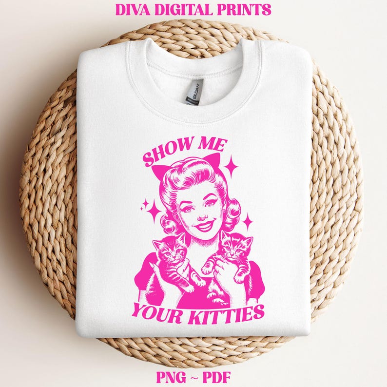 May include: A white t-shirt with a pink graphic of a woman with two kittens. The text "Show Me Your Kitties" is printed in pink on the shirt.