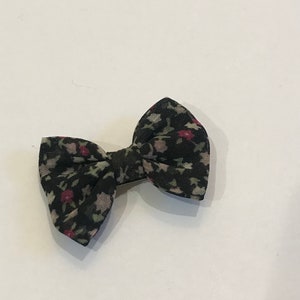 May include: A small black bow with a floral print in shades of pink, green, and white.