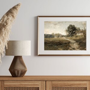 Peut inclure: Une peinture de paysage encadr&eacute;e repr&eacute;sentant une sc&egrave;ne rurale avec un chemin de terre menant &agrave; une ferme au loin. La peinture est dans des tons de brun, vert et gris, avec un ciel nuageux en arri&egrave;re-plan.