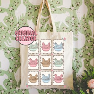 May include: A cream-colored tote bag featuring a repeating pattern of postage stamp-style illustrations of chickens in pastel-colored bowls. The text "ORIGINAL CREATOR" is in a pink circle. The bag has a simple design with long handles.