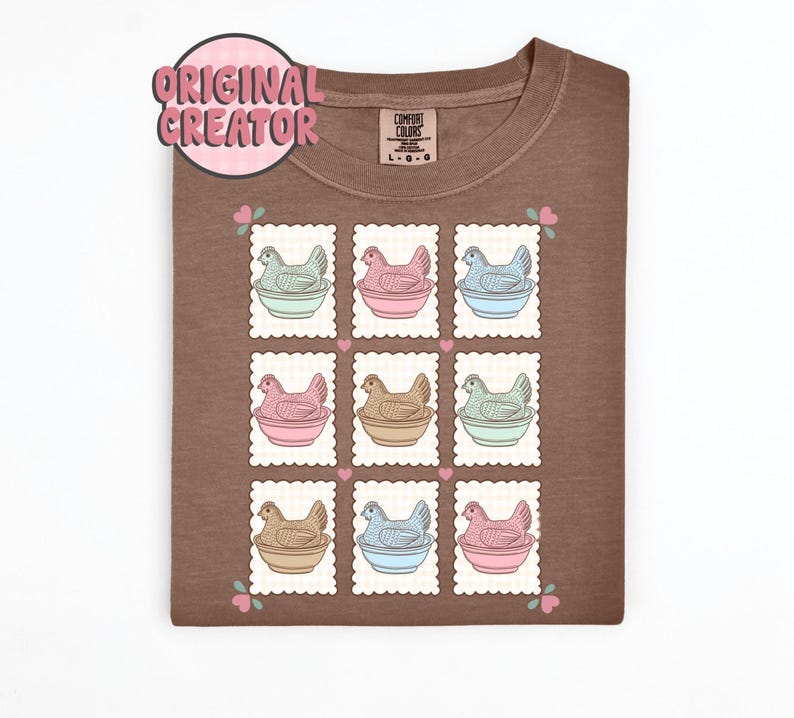 May include: Brown t-shirt featuring a grid of nine postage stamp-style illustrations. Each stamp depicts a hen in a bowl, with varying pastel colors. The shirt has a tag that says "Comfort Colors" and a pink "Original Creator" logo.