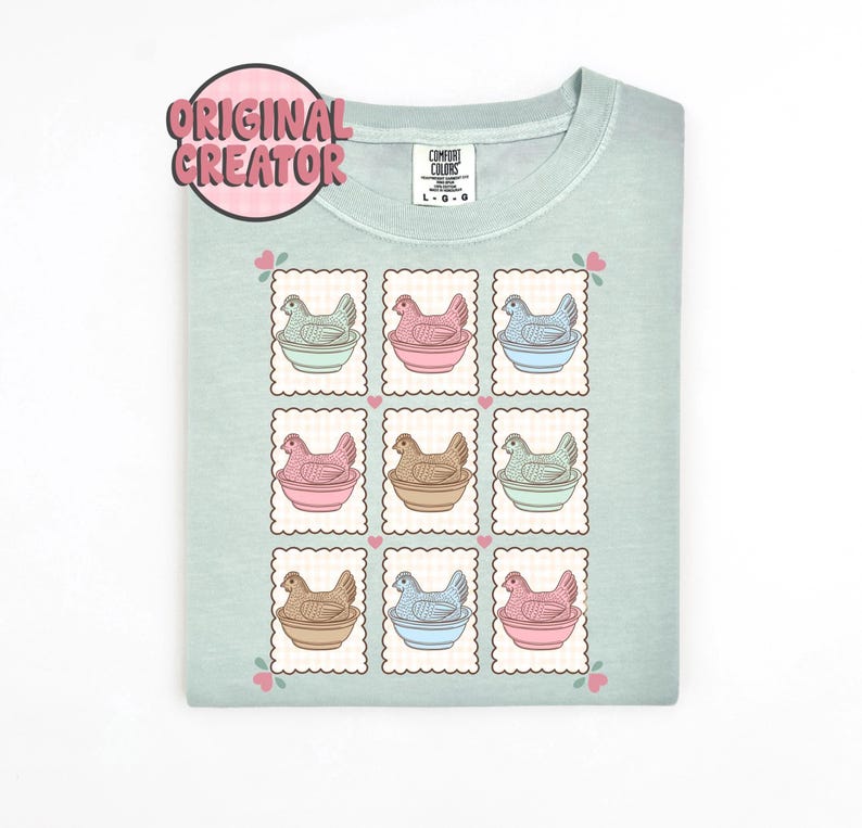 May include: A light green t-shirt featuring a grid of nine postage stamp-style illustrations. Each stamp depicts a hen in a bowl, with varying colors of pink, blue, brown, and green. The shirt has the text "ORIGINAL CREATOR" in a pink circle.