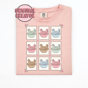 May include: A light pink crew neck sweatshirt with a repeating pattern of chicken illustrations in pastel colors. Each chicken is in a bowl, framed by a postage stamp design. The text "ORIGINAL CREATOR" is in a pink circle.