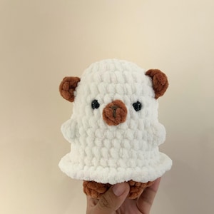 May include: White crocheted plush toy with brown ears and a brown nose. The toy is shaped like a bear and has black eyes.
