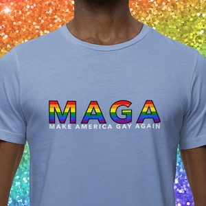 May include: A light blue t-shirt with the text "Maga" in rainbow colors. The text is outlined in black and the words "Make America Gay Again" are written below the rainbow text.