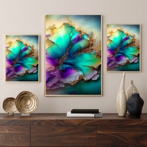 May include: Three framed abstract art prints with gold frames. The artwork features a vibrant floral design in shades of teal, purple, and gold. The prints are displayed on a dark wood cabinet, alongside decorative objects.