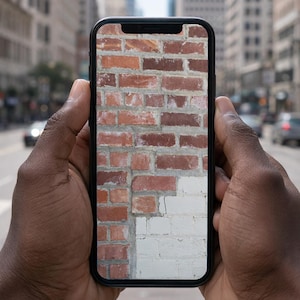 May include: A black smartphone displaying a high-resolution image of a brick wall on its screen. The wall features a mix of weathered red bricks and a section of white painted bricks, showing distinct textures and mortar lines in the masonry.