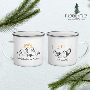 May include: Two white enamel mugs with black and gold mountain illustrations. The mug on the left says "The Mountains are Calling..." and the mug on the right says "...and I must Go."