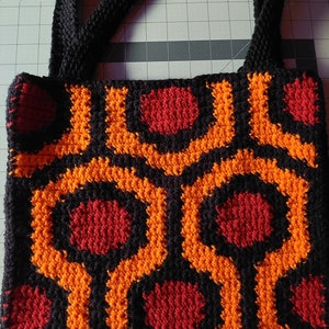 May include: A black crocheted tote bag with a repeating pattern of orange and red circles. The bag has two black straps.