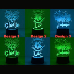 May include: A collection of three illuminated night lights with personalized names. Design 1 features a heart-shaped design with the name "Charlie". Design 2 displays the Hogwarts crest with the name "Lily". Design 3 shows a castle with the name "Jolene". Each light has a black base.