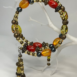 Könnte beinhalten: Ein mehrreihiges Armband mit orangefarbenen, gelben und braunen Perlen. Das Armband hat einen Anhänger mit ähnlichen Perlen.