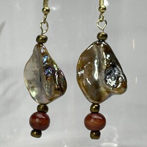 May include: A pair of gold dangle earrings with iridescent shell-shaped pendants and brown wooden beads.