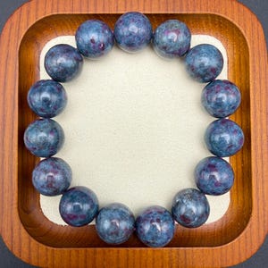 May include: A circular bracelet composed of fifteen polished, spherical beads. Each bead features a deep blue base color with mottled, dark red and purple inclusions throughout the stone surface, creating a varied, natural appearance in every bead.
