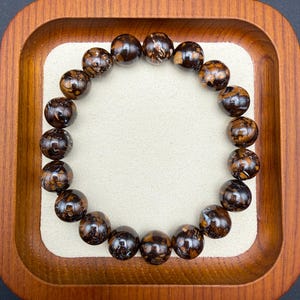 May include: A circular bracelet composed of nineteen spherical beads. Each bead features a polished, dark brown surface with intricate, swirling patterns of lighter tan and cream-colored inclusions, creating a marbled appearance throughout the piece.