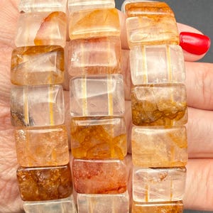 May include: Three bracelets made of rectangular, translucent beads with orange and brown inclusions. The beads are strung together, forming a flexible band. The bracelets are held in a hand, with the letters A, B, and C visible.