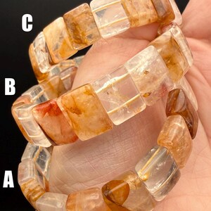 May include: Three gemstone bracelets with rectangular, translucent beads in shades of amber, orange, and clear. The bracelets are stacked, showcasing the variations in color and clarity of the stones. The bracelets are held in a hand.