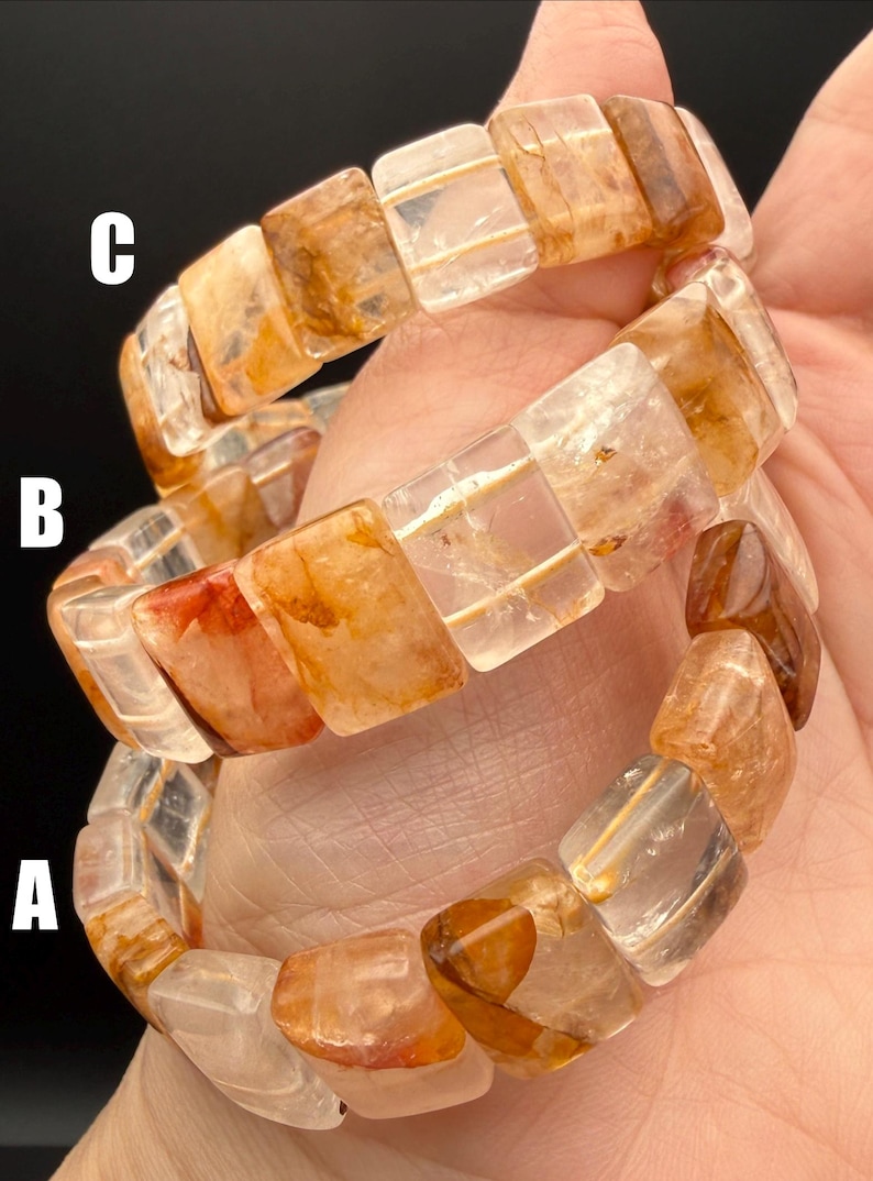 May include: Three gemstone bracelets with rectangular, translucent beads in shades of amber, orange, and clear. The bracelets are stacked, showcasing the variations in color and clarity of the stones. The bracelets are held in a hand.