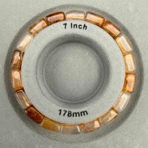 May include: A beaded bracelet with rectangular, amber-colored stones. The bracelet is 7 inches in length and is displayed on a gray surface. The text "7 inch" is visible on the surface.