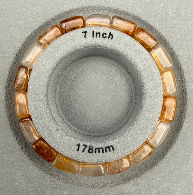 May include: A beaded bracelet with rectangular, amber-colored stones. The bracelet is 7 inches in length and is displayed on a gray surface. The text "7 inch" is visible on the surface.