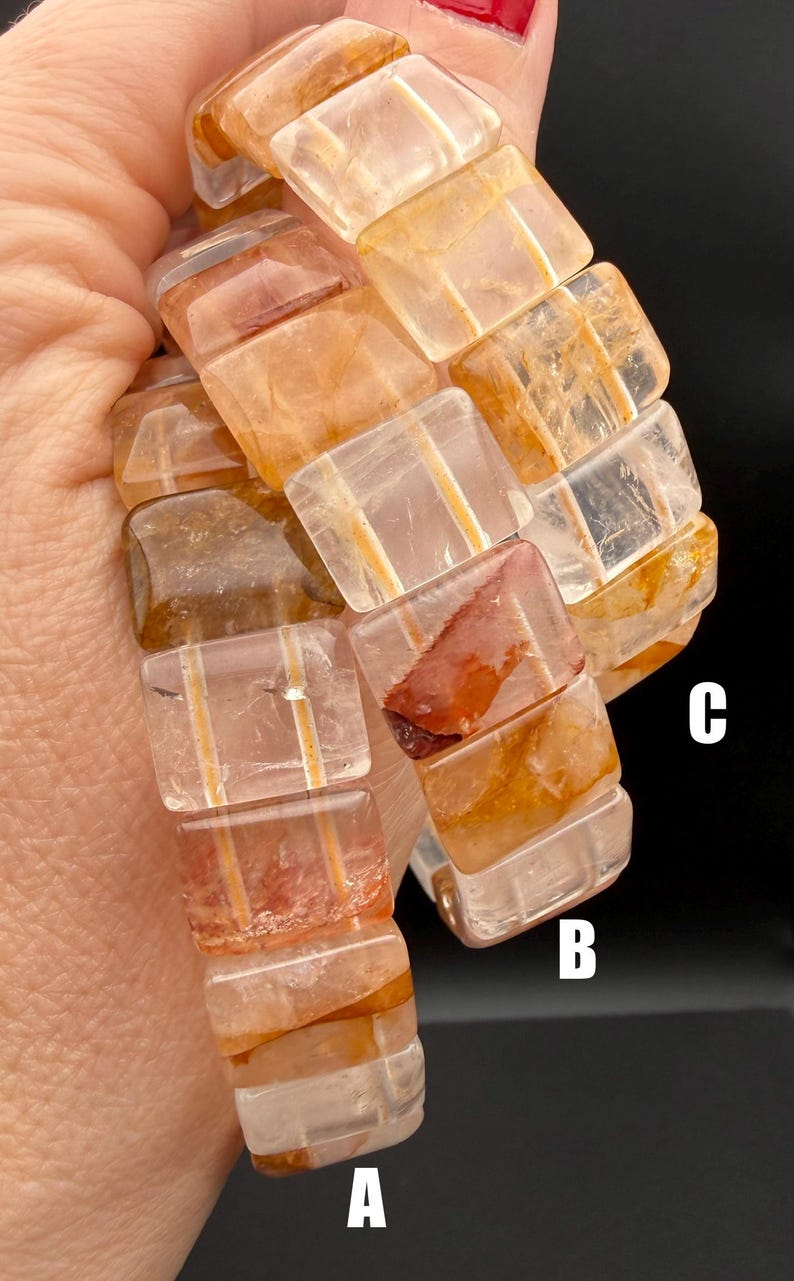 May include: A close-up of a bracelet made of rectangular, translucent, orange-brown gemstones. The bracelet is held against a dark background. The gemstones have internal striations and variations in color.