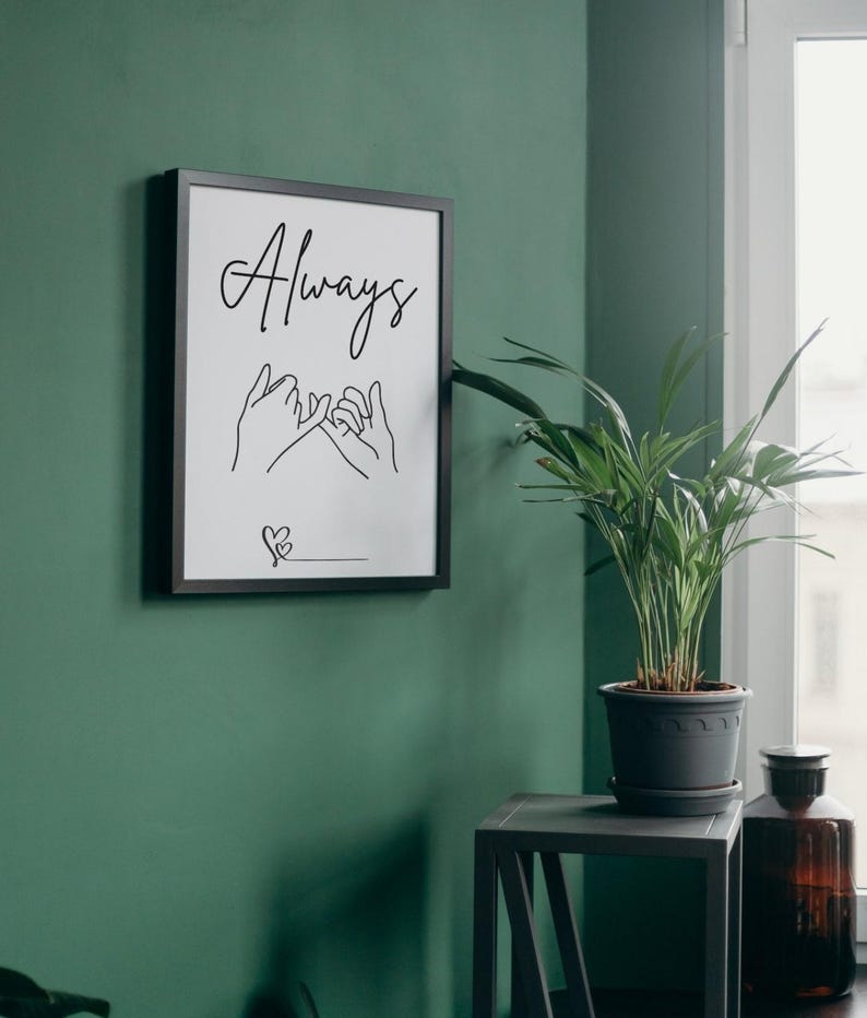 May include: A black framed print with the word "Always" written in cursive. Two hands are drawn with intertwined pinky fingers, and a small heart is drawn below. The print is hanging on a green wall.
