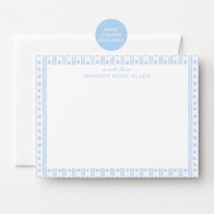 May include: A white stationery card with a light blue border featuring a repeating pattern of small flowers and vertical stripes. The text "a note from MARGOT ROSE ALLEN" is printed in light blue in the center. A matching white envelope is behind it.