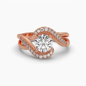 Puede incluir: Anillo de compromiso de oro rosa con una piedra central redonda y transparente. El anillo presenta un halo de piedras m&aacute;s peque&ntilde;as alrededor del centro y a lo largo de la banda en espiral. El dise&ntilde;o es elegante y moderno.