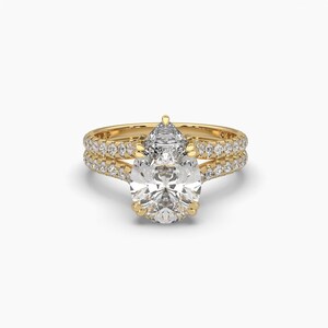 Puede incluir: Un juego de anillos de compromiso de oro con una piedra central de diamante en forma de pera y una banda a juego. Las bandas est&aacute;n adornadas con numerosos diamantes peque&ntilde;os y brillantes, creando una apariencia lujosa y elegante. El anillo est&aacute; sobre un fondo blanco.