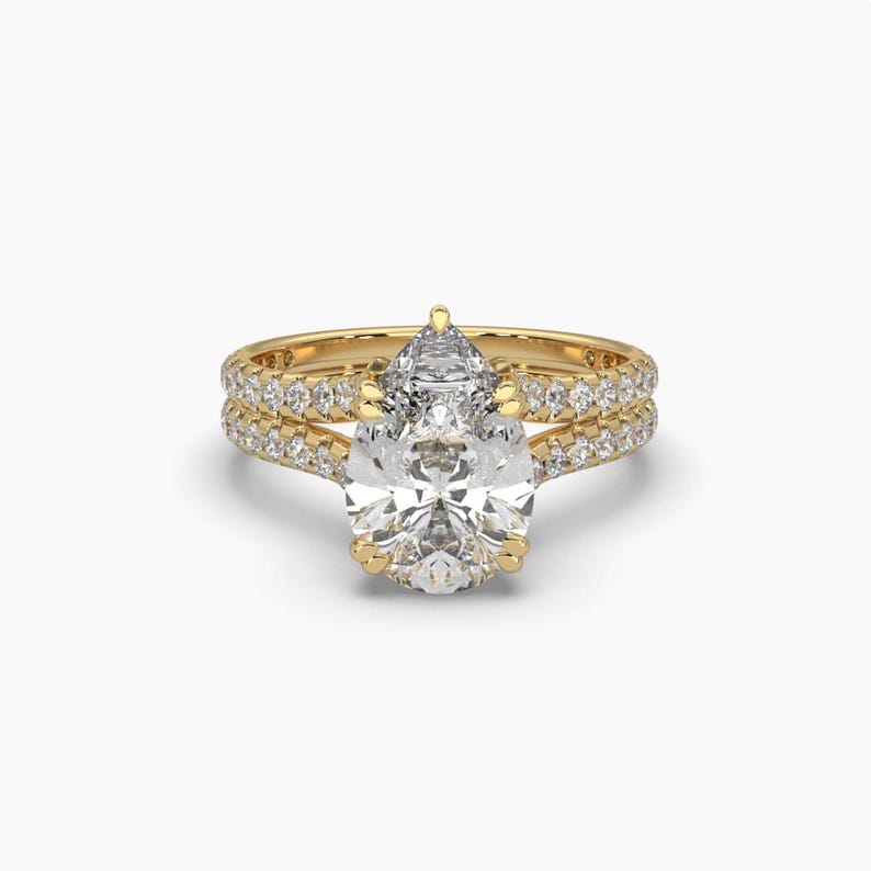 Puede incluir: Un juego de anillos de compromiso de oro con una piedra central de diamante en forma de pera y una banda a juego. Las bandas est&aacute;n adornadas con numerosos diamantes peque&ntilde;os y brillantes, creando una apariencia lujosa y elegante. El anillo est&aacute; sobre un fondo blanco.