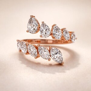 Puede incluir: Un anillo de oro rosa con un dise&ntilde;o en espiral adornado con piedras preciosas claras y brillantes. El anillo presenta una serie de piedras en forma de pera y marquesa, creando una est&eacute;tica lujosa y elegante. Las piedras est&aacute;n engastadas en un engaste delicado.