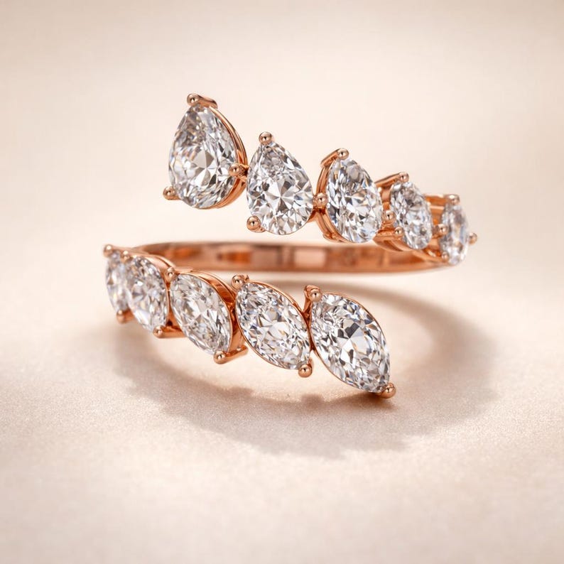 Puede incluir: Un anillo de oro rosa con un dise&ntilde;o en espiral adornado con piedras preciosas claras y brillantes. El anillo presenta una serie de piedras en forma de pera y marquesa, creando una est&eacute;tica lujosa y elegante. Las piedras est&aacute;n engastadas en un engaste delicado.
