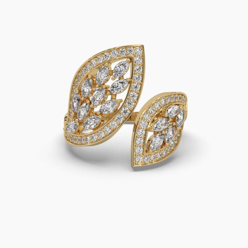 Puede incluir: Un anillo dorado con un dise&ntilde;o en forma de hoja. El anillo presenta una gran forma de hoja abierta adornada con numerosas piedras preciosas claras y brillantes. Los bordes de las hojas est&aacute;n bordeados con piedras preciosas m&aacute;s peque&ntilde;as, realzando el brillo general.