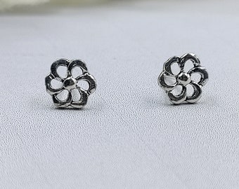 May include: A pair of silver flower stud earrings. The earrings are small and delicate, with a simple design.