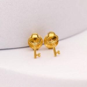 Puede incluir: Un par de pendientes dorados con forma de llave. Los pendientes tienen un diseño detallado, con una parte superior en forma de ojo de cerradura y un pequeño lazo decorativo en la parte inferior. Sobre fondo blanco.