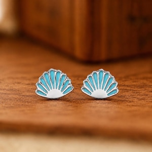 May include: A pair of silver stud earrings shaped like seashells, featuring a bright turquoise enamel inlay within the fan-like ridges of the shell design. The earrings have a polished metallic finish and a classic post-back style construction.