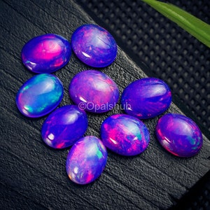 May include: A collection of eight oval-shaped opals with a variety of iridescent colors, including purple, blue, and pink. The opals are arranged on a black surface.