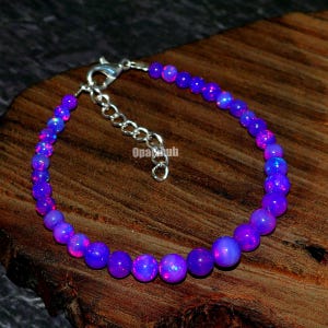 May include: A purple and pink opal beaded bracelet with a silver clasp. The bracelet is made of small, round beads that are strung together on a silver chain.