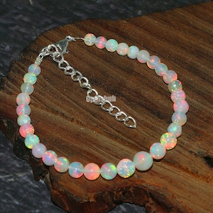 May include: A silver chain bracelet with a clasp fastening. The bracelet is made of white opal beads with iridescent rainbow colours.
