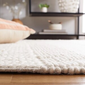 May include: Close-up of a white, fluffy rug with a textured surface. The rug has a subtle pattern of small bumps and is made of a soft, plush material.