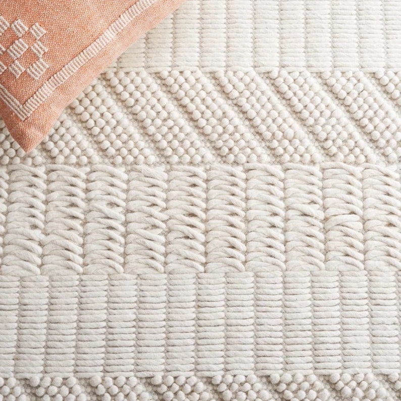 May include: A close-up of a white woven rug with a textured pattern. The rug has a raised, bumpy texture and a subtle geometric design.