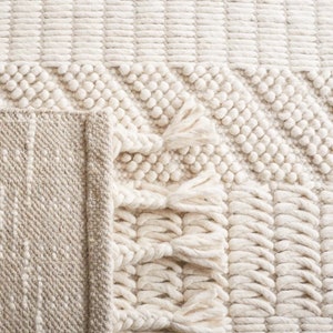 May include: A white woven rug with a textured pattern and fringe. The rug has a subtle beige border.